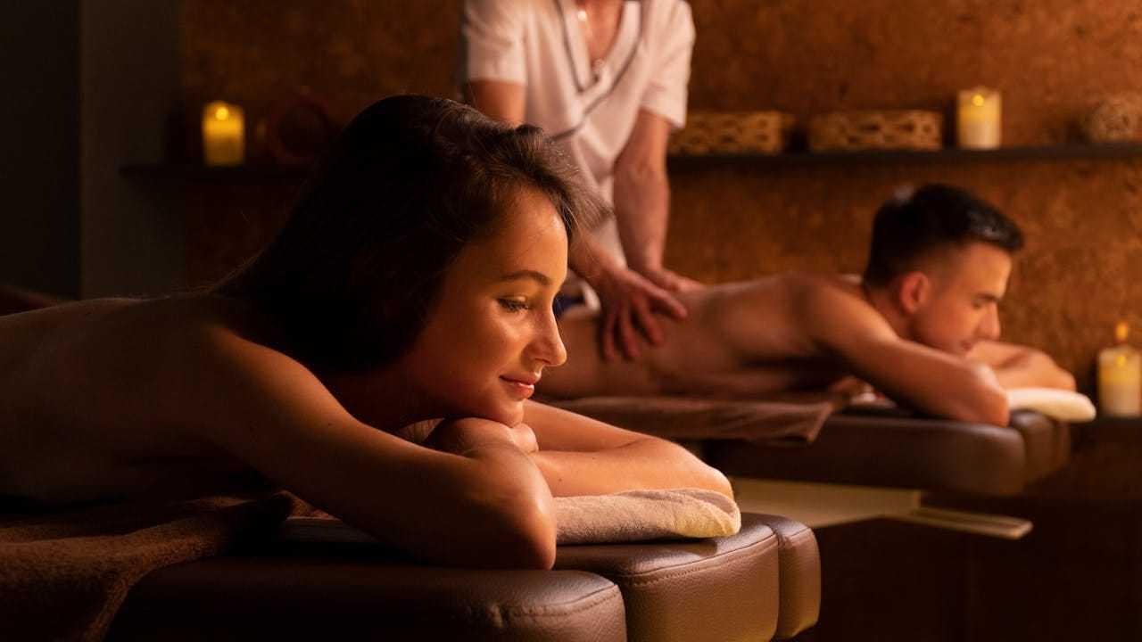 Couple enjoying relaxing back massages in a peaceful, candle-lit spa setting.